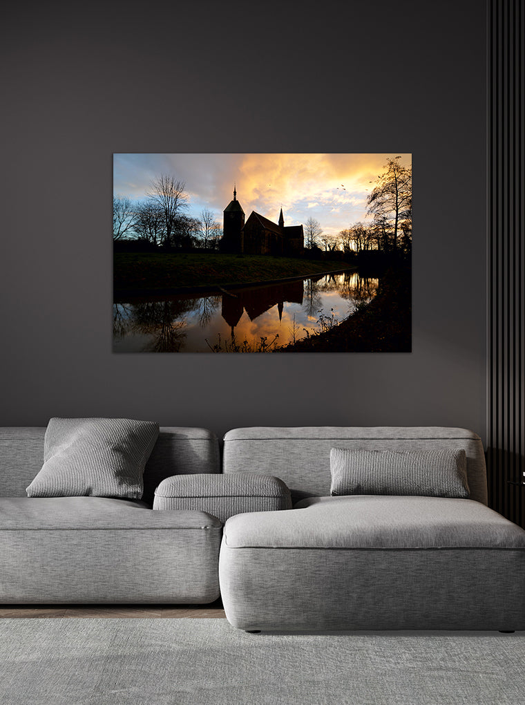 Darstellung eines Art Prints der Heimatlinse hängend an einer Wand in dunkler Umgebung mit Motiv von Kirchen-Silhouetten bei Abendstimmung.