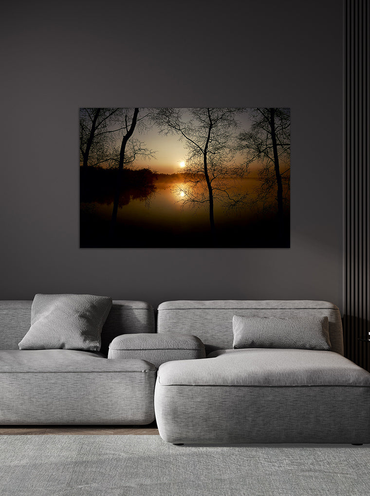 Darstellung eines Art Prints der Heimatlinse hängend an einer Wand in dunkler Umgebung mit Motiv eines Sonnenaufgangs und dunklen Silhouetten am See.
