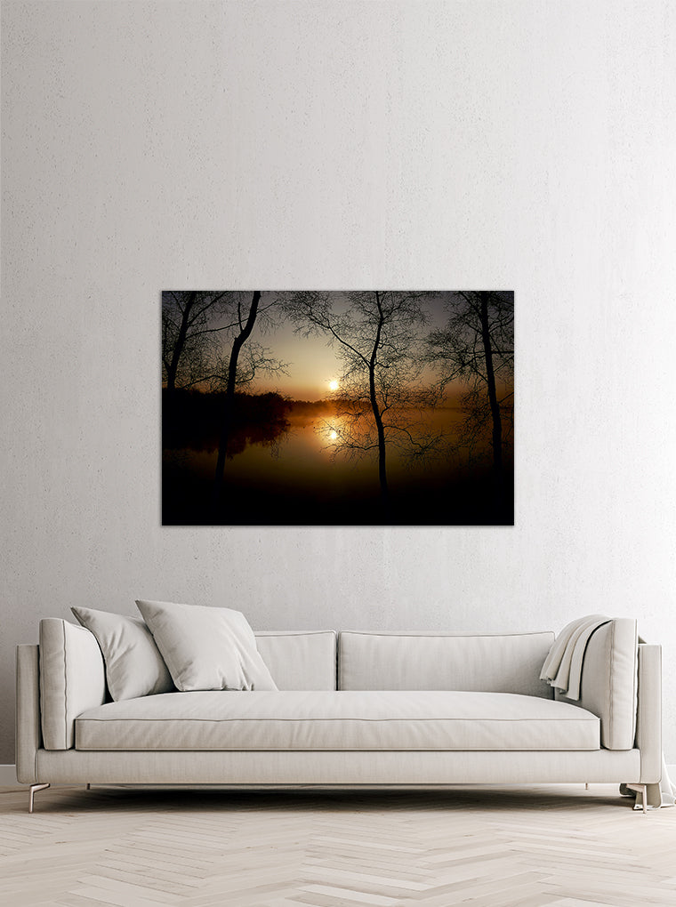 Darstellung eines Art Prints der Heimatlinse hängend an einer Wand in heller Umgebung mit Motiv eines Sonnenaufgangs und dunklen Silhouetten am See.