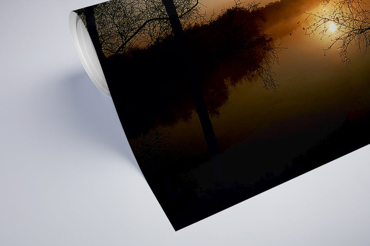 Darstellung eines Art Prints der Heimatlinse als halb aufgerolltes semi-mattes Poster mit Motiv eines Sonnenaufgangs und dunklen Silhouetten am See.