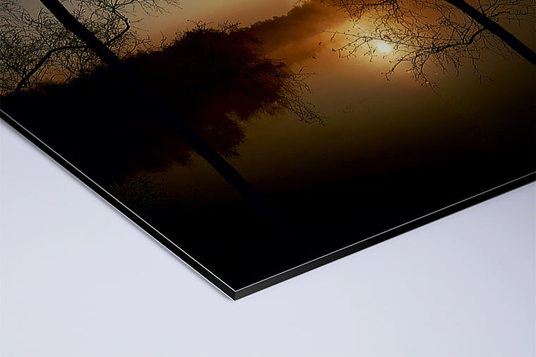 Darstellung eines Art Prints der Heimatlinse als matter UV-Direktdruck auf Aluverbund mit Motiv eines Sonnenaufgangs und dunklen Silhouetten am See.