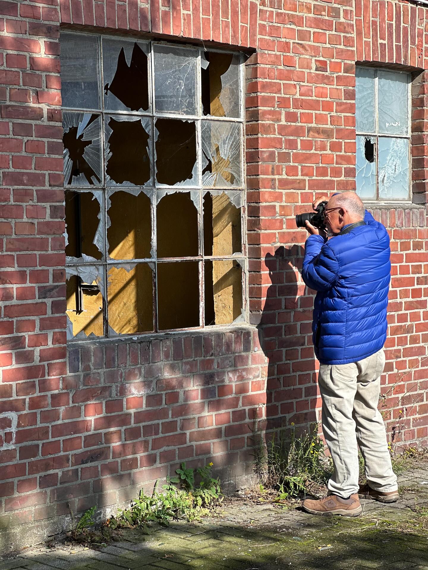 Hubert Stroetmann, wie er draußen vor einem Gebäude durch eine zerbrochene Fensterscheibe fotografiert.