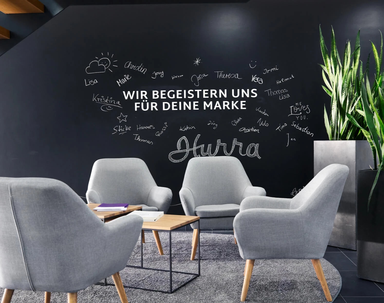 Gemütliche Sitzecke im Eingangsbereich der Firma KruseMedien in Vreden vor einer Kreidewand, die mit den Namen der Mitarbeiter beschriftet ist.